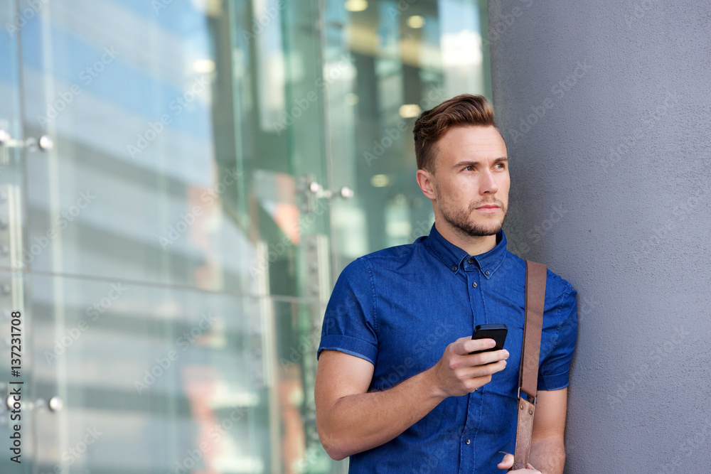 handsome young man leaning against wall outside with cellphone handsome young man leaning against wall outside with cellphone