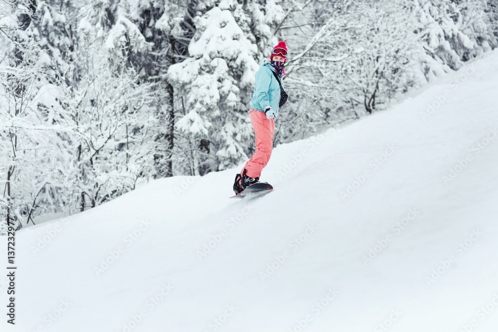 Woman in ski suit looks over her shoulder going down the hill on her snowboard