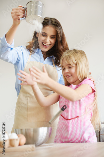 Mother and daughter baking together, sieving flour, fooling around