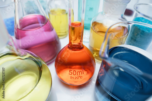 Volumetric flask containing solution of potassium dichromate (VI) (K2Cr2O7) and other flasks of transition metal salts, dry chemicals and solutions. Compounds with transition metals are often colored photo