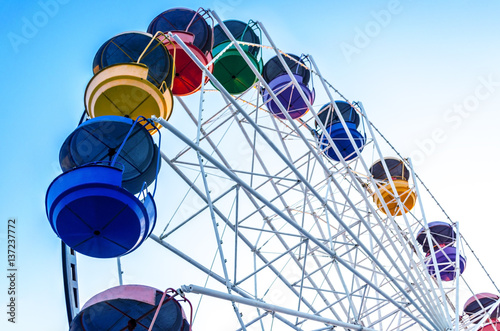 old Ferris wheel with colored cabins open against the blue sky