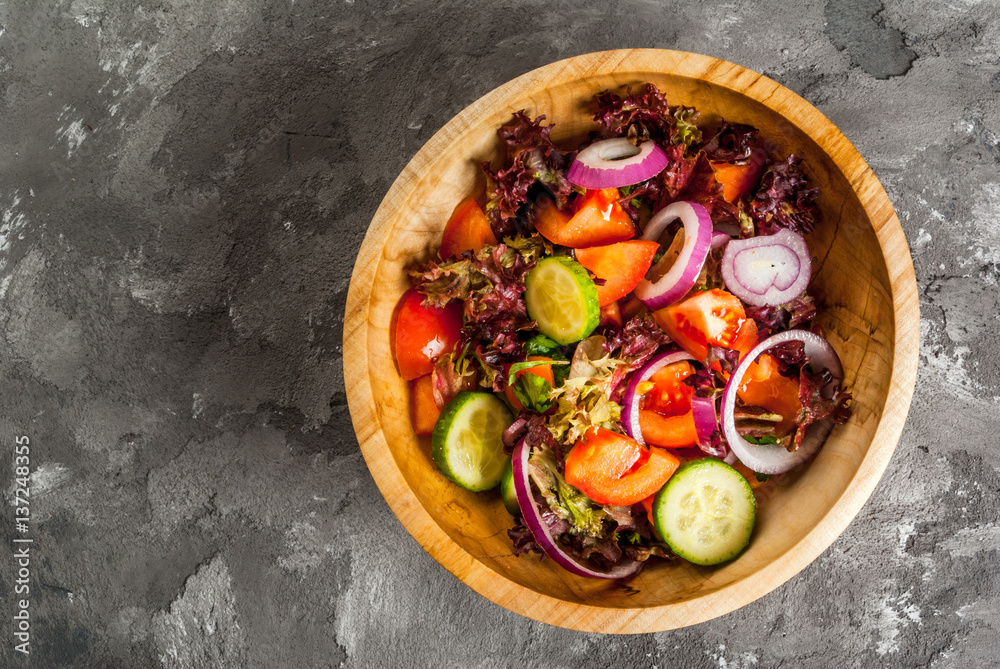 Salad of fresh spring vegetables and lettuce leaves in a wooden bowl on a concrete stone gray table, top view, copy space