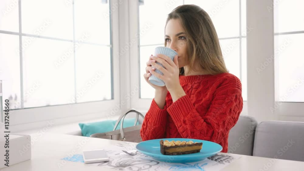 Smiling Woman in sweater sitting by the table and drinking coffee in cafe Smiling Woman in sweater sitting by the table and drinking coffee in cafe