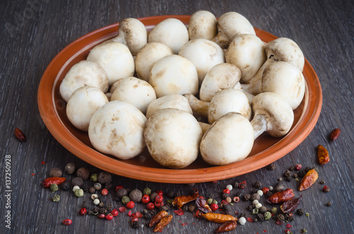 Fresh mushrooms with spices on plate, wooden background