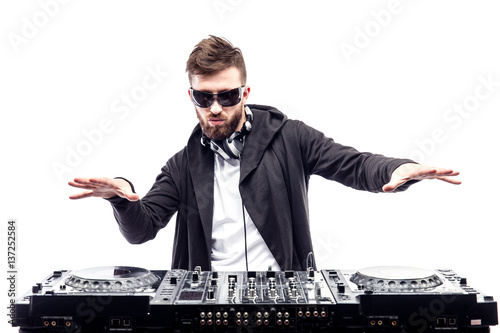 Young stylish man in black sunglasses posing with hands up behind mixing console on white studio background.