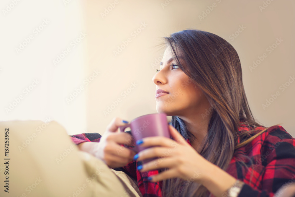 Attractive young woman drinking coffee at home looking to the window and daydreaming