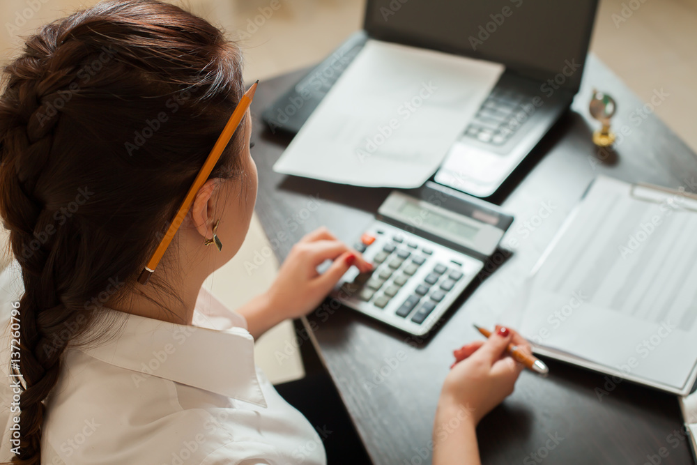 Young female bookkeeper considers on calculator - obrazy, fototapety, plakaty 