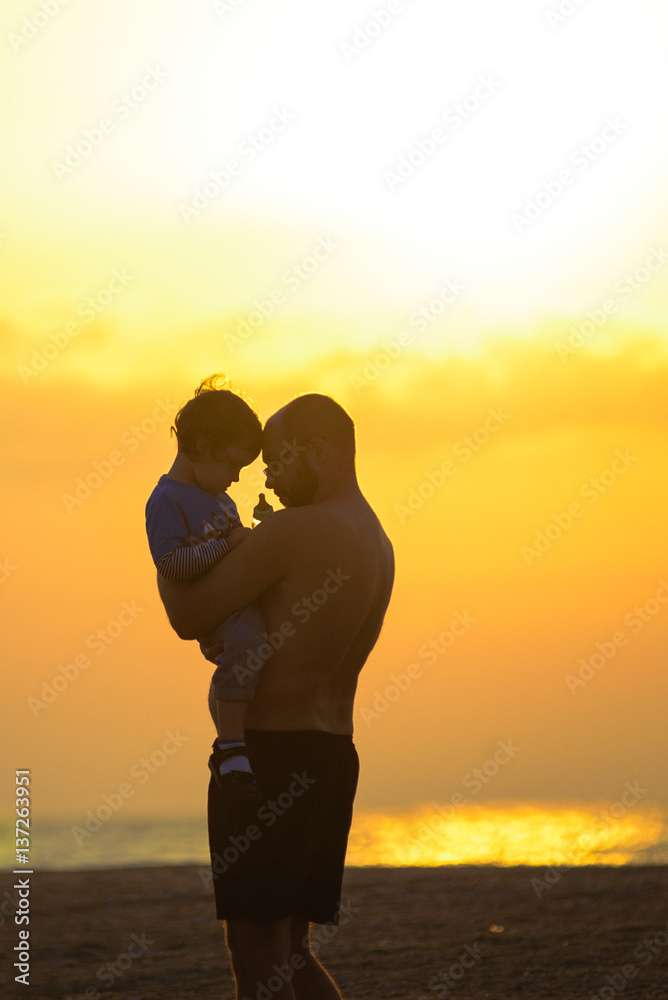 Silhouette of small baby with father during sunset.