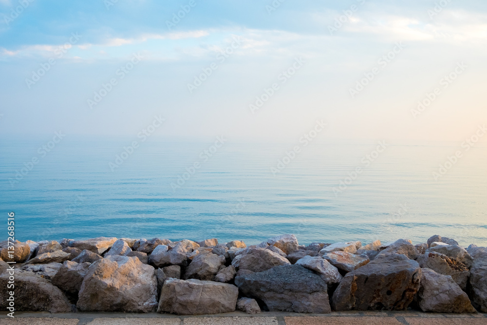 peaceful quiet rock pier at sunrise with calm blue sea waves