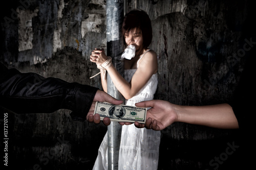 Human trafficking concept., Person hand with a dollar banknote buying victim woman in pain and bound hands with rope., missing kidnapped., in dark tone.