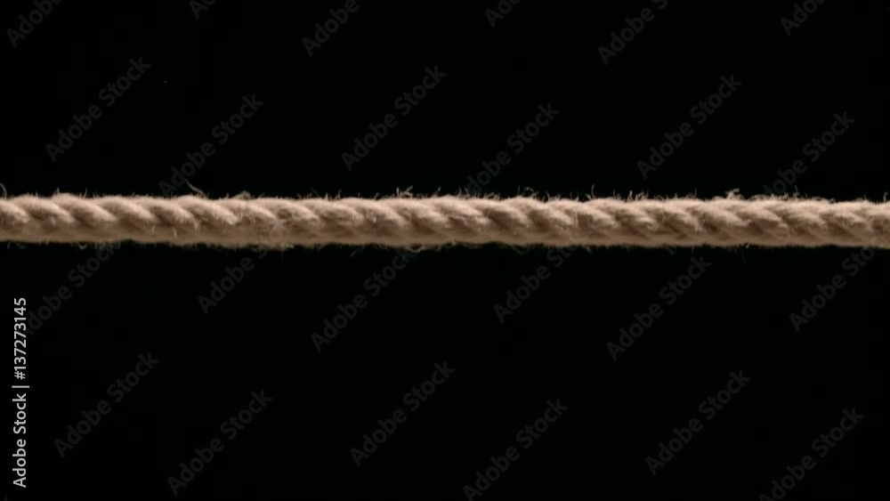 Close up of rope being pulled taut into frame against black Close up of rope being pulled taut into frame against black