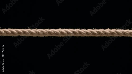 Close up of rope being pulled taut into frame against black