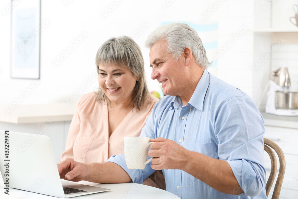 Middle aged couple with laptop at kitchen Middle aged couple with laptop at kitchen