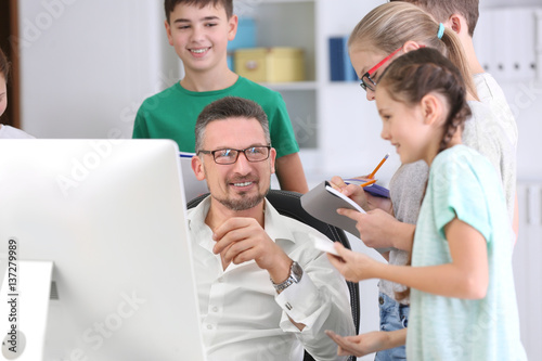 Male teacher working with computer while conducting lesson in classroom