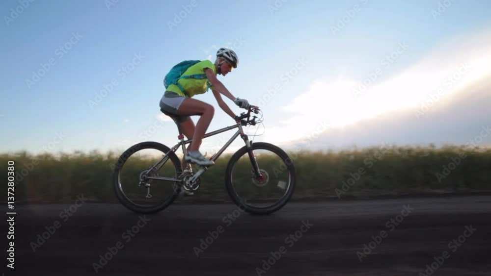 Woman cyclist rides bike a dirt road, rear view Woman cyclist rides bike a dirt road, rear view