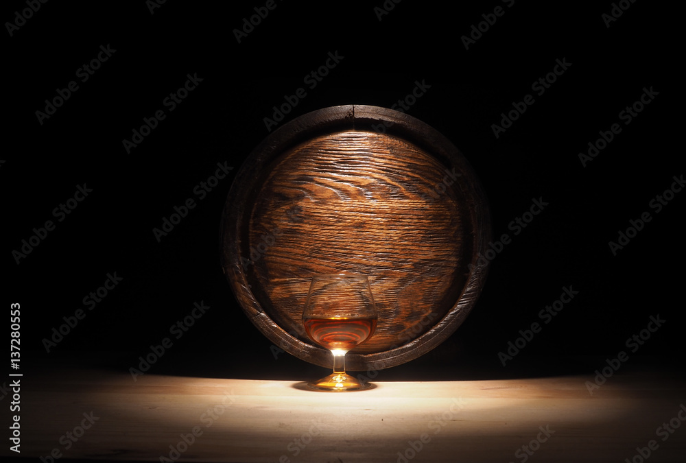 Glass of cognac with barrel on wooden backgroun