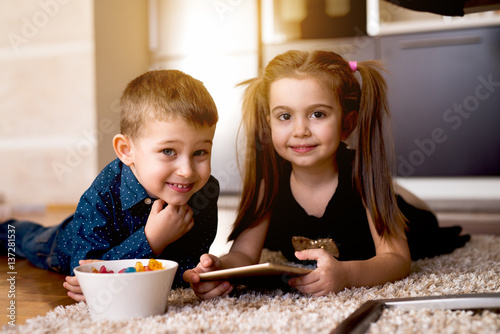 Adorable kids playing on tab togeher, having tasty gelly snacks.
