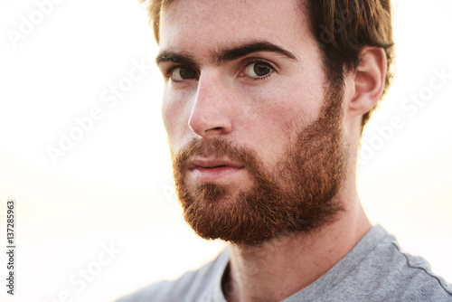 close up face shot of white bearded male looking straight into camera with serious facial expression.