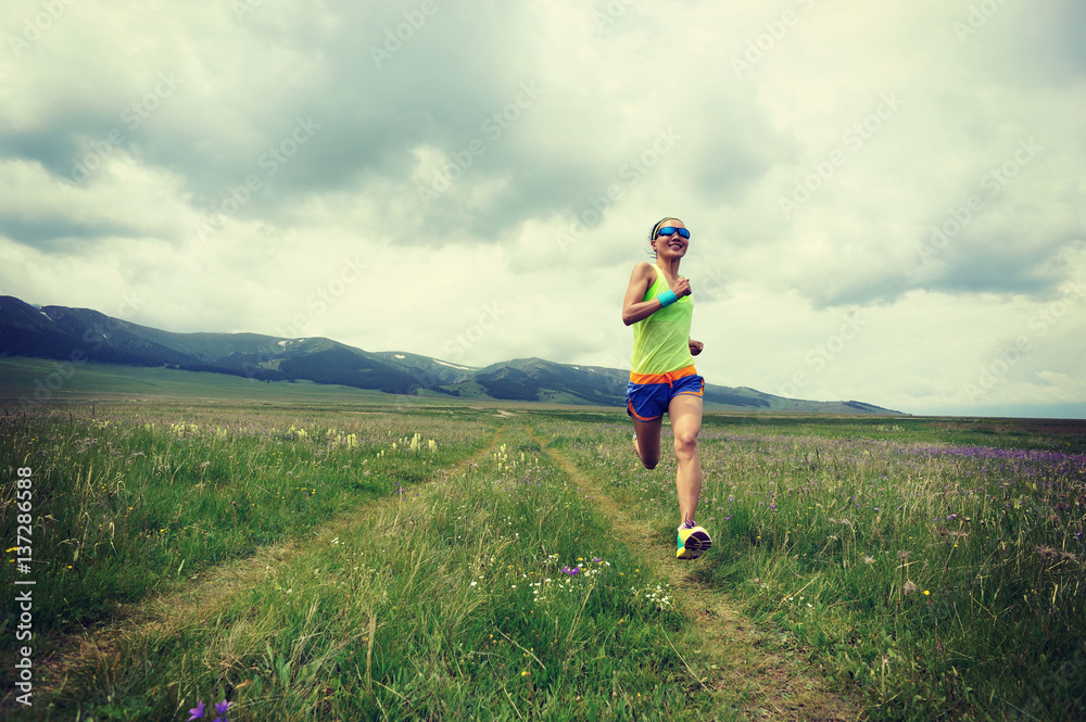 young fitness woman trail runner running on grassland