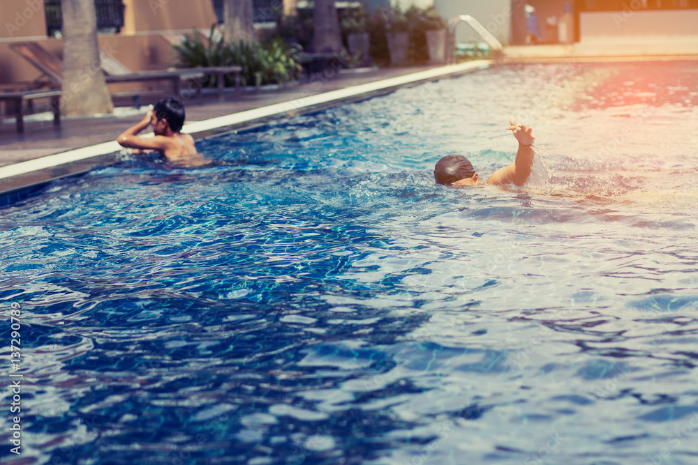 boy playing and swimming in swimming pool ; feeling joyful with his friend