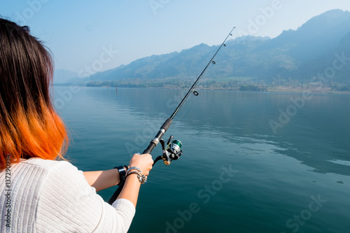 beautiful girl holding fishing rod, fishing pole over the lake.