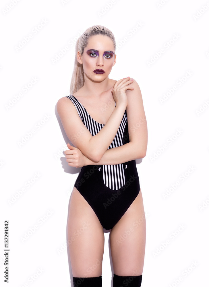 Portrait of young beautiful woman dressed in striped swimsuit posing near wall Portrait of young beautiful woman dressed in striped swimsuit posing near wall