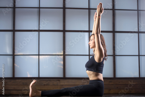Young attractive woman practicing yoga, sitting in Staff exercise, Dandasana pose, working out, wearing sportswear, black tank top, pants, indoor full length, studio evening practice