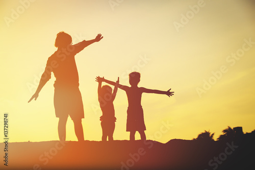 father with son and daughter silhouettes play at sunset