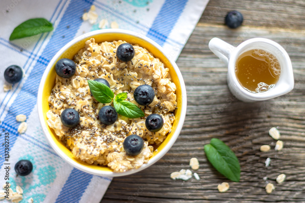 Porridge - Oat Flakes with Blueberries and Mint Leaves on Wooden Background with Blue and White Tablecloth