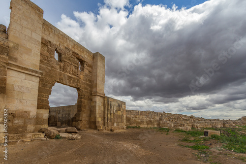 Photo of historic Harran University gates. Photo taken with wide angle lens from side. Enterance of the gate in front, with dusty roar aproaching to gate. Blue sky with clouds in the background.