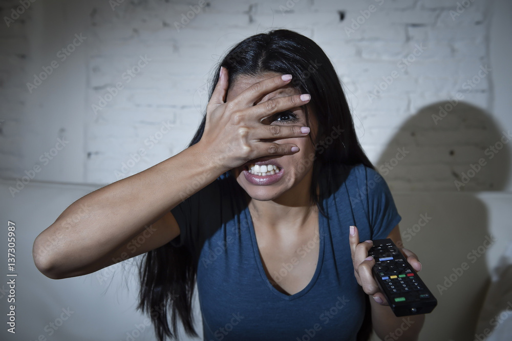 Fototapeta premium latin woman at home sofa couch in living room watching television covering eyes horrified
