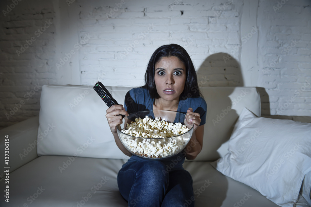 Fototapeta premium latin woman at home sofa couch in living room watching television covering eyes horrified