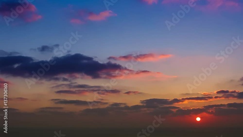 time lapse of clouds crossing the amazing sky over the sea or ocean at sunset. transition from day to night. The clouds cross slowly from left to right colored yellow orange purple blue.