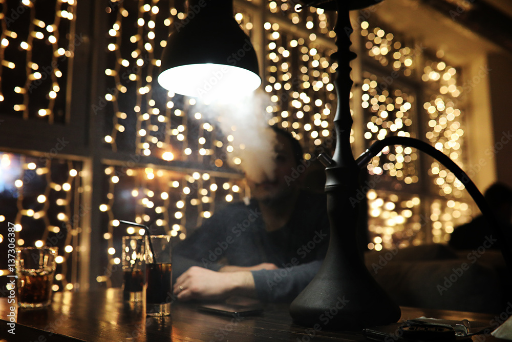 man holding hookah pipe and smoking in a night club man holding hookah pipe and smoking in a night club