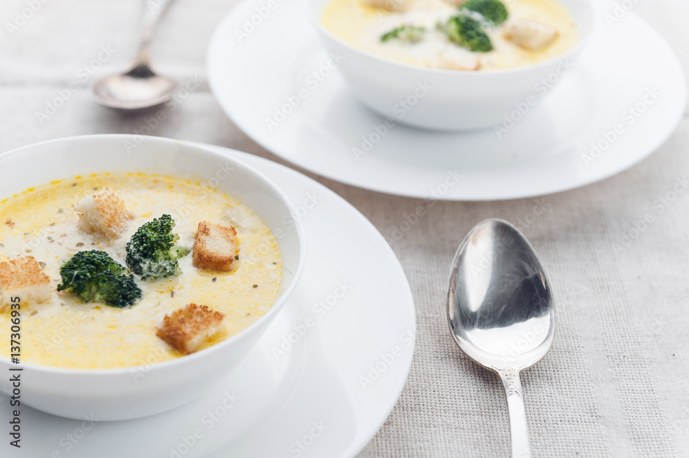 cheese soup with broccoli in a white plate on a white linen tablecloth