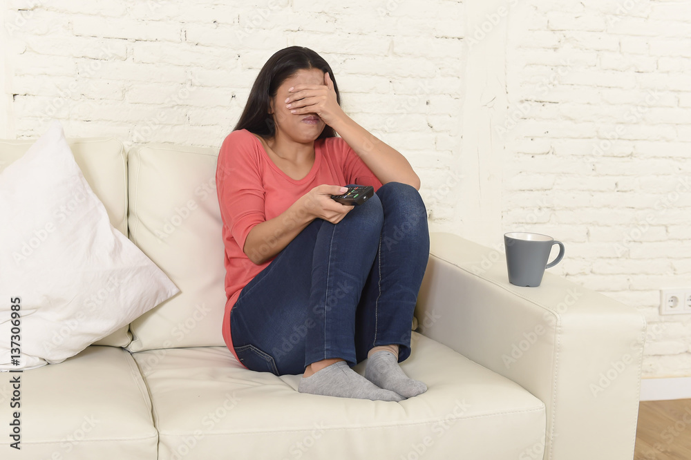 Naklejka premium latin woman sitting at home sofa couch in living room watching television scary horror movie