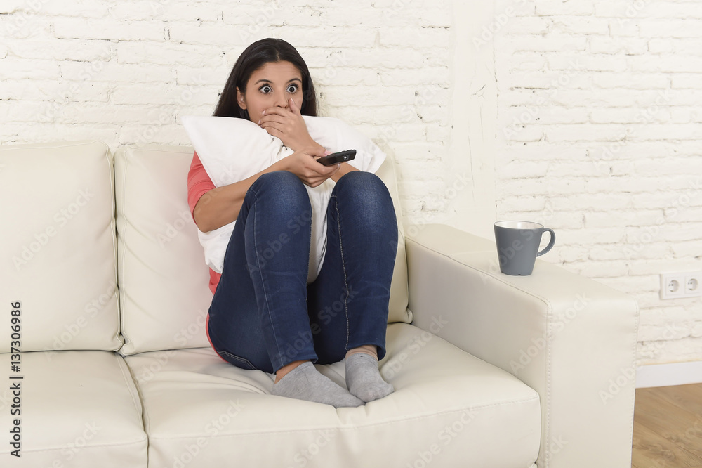 Naklejka premium latin woman sitting at home sofa couch in living room watching television scary horror movie