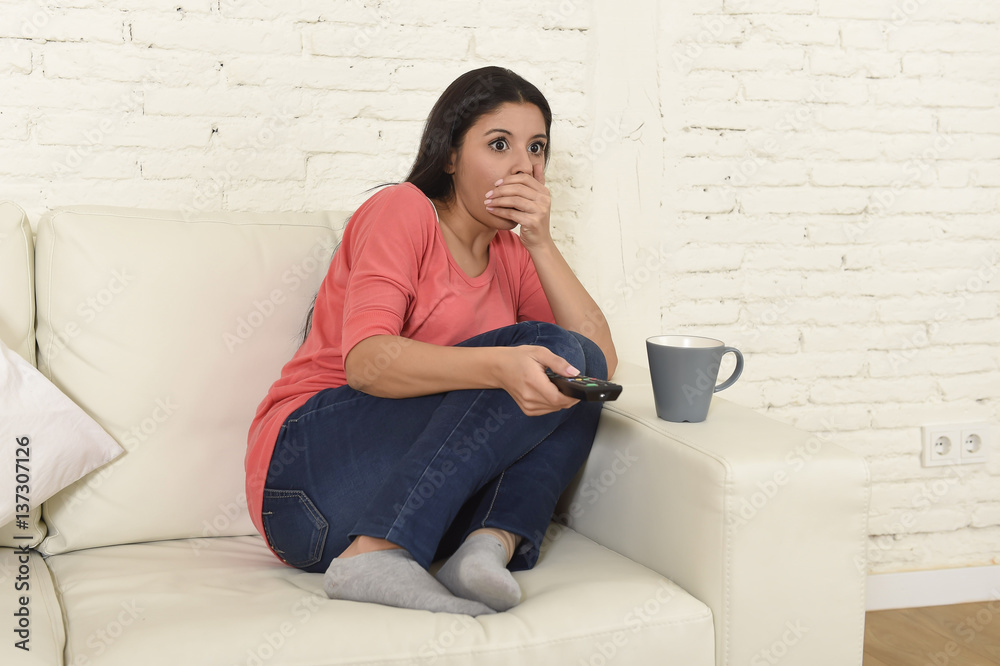 Naklejka premium latin woman sitting at home sofa couch in living room watching television scary horror movie