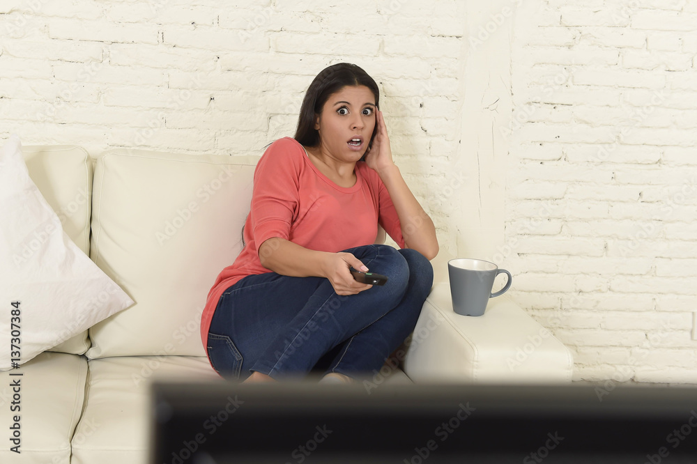 Fototapeta premium latin woman sitting at home sofa couch in living room watching television scary horror movie