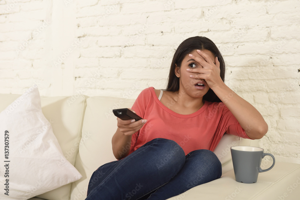 Fototapeta premium latin woman sitting at home sofa couch in living room watching television scary horror movie