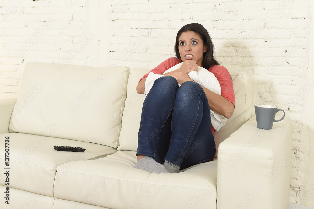 Naklejka premium latin woman sitting at home sofa couch in living room watching television scary horror movie