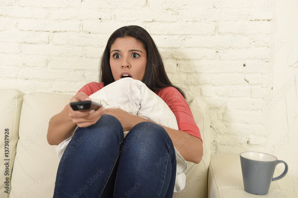 Naklejka premium latin woman sitting at home sofa couch in living room watching television scary horror movie