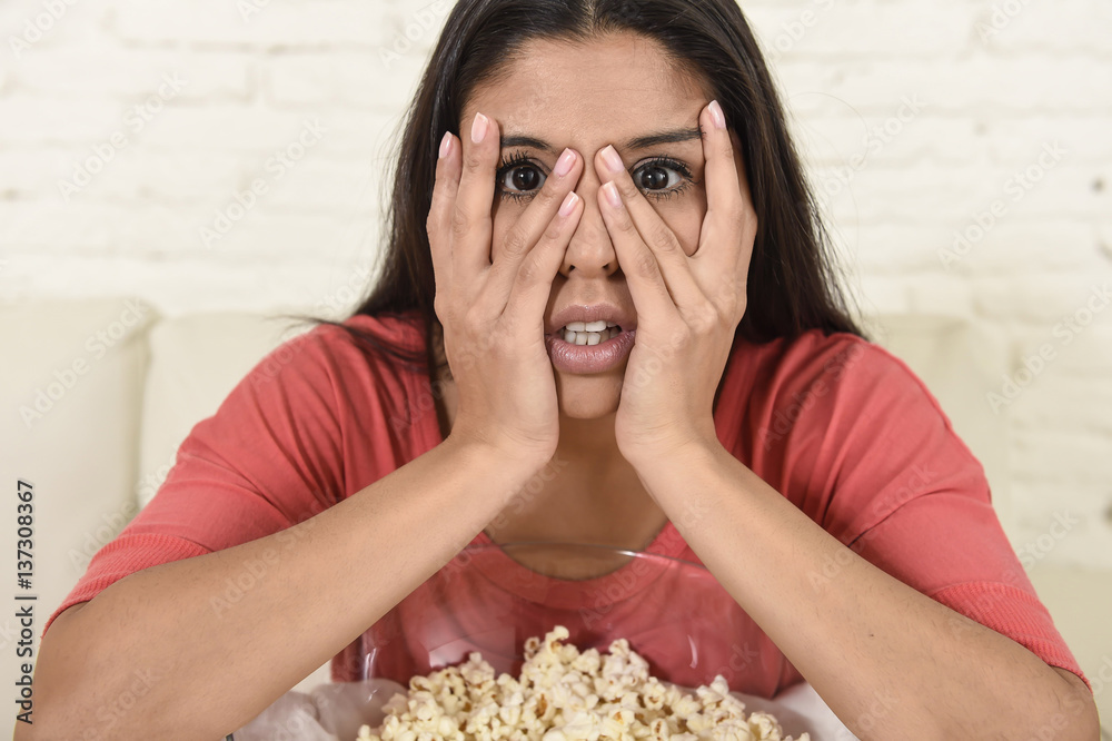 Naklejka premium latin woman sitting at home sofa couch in living room watching television scary horror movie