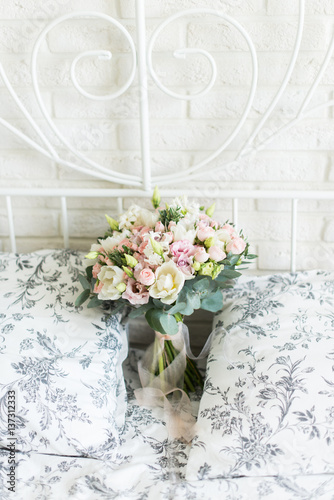 Wedding bouquet with white and pink tulips and pink small roses on a bridal bed with black and white bedclothes on a brick background
