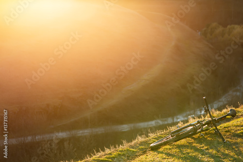 Mountain bicycle is on the hill with green grass on sunset background.