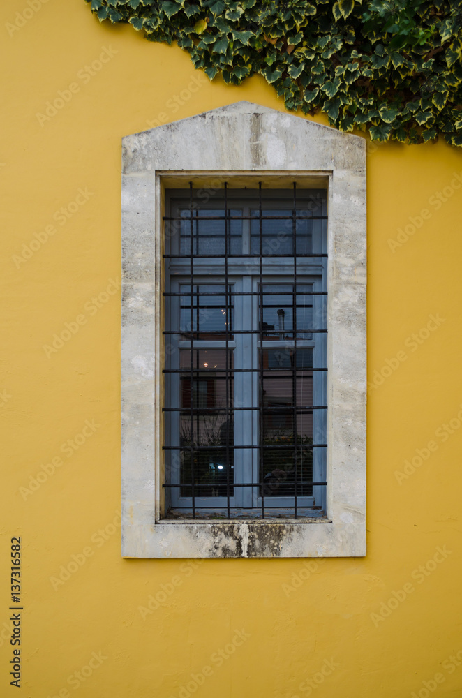 old wooden window with marble frame on a yellow wall and a plant on the top. The building is located in the colorful and awarded village of Crete, Archanes