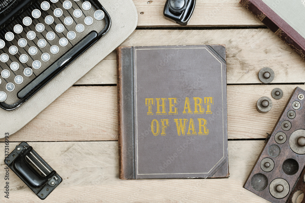 The Art of War on old book cover at office desk with vintage items