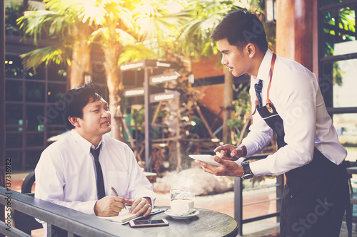 Young handsome waiter with touch pad waiting for businessman order in coffee shop
