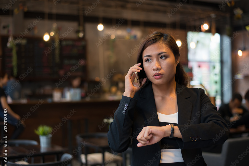 Beautiful business woman talking on cell phone looking at hand watch over cafe background. Beautiful business woman talking on cell phone looking at hand watch over cafe background.