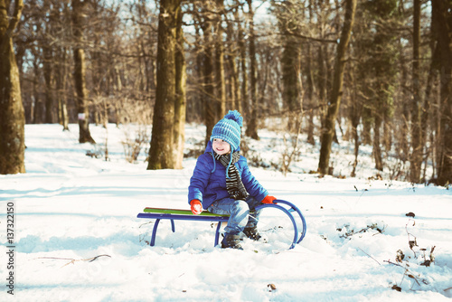Little boy enjoying a sleigh ride. Child sledding. Toddler kid riding a sled. Children play outdoors in snow. Kids sled in winter park. Outdoor active fun for family vacation.